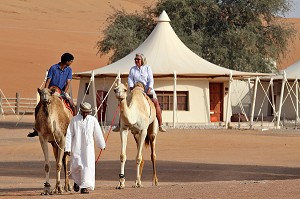TOURISTE INDIEN ET TOURISTE BRITANNIQUE FAISANT UN TOUR A DOS DE DROMADAIRES DANS L'ENCEINTE DU COMPLEXE TOURISTIQUE DESERT NIGHT CAMP, DESERT DE WAHIBA SANDS, SULTANAT D'OMAN, MOYEN-ORIENT 