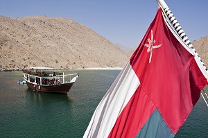 DRAPEAU NATIONAL OMANAIS ET BOUTRE TRADITIONNEL MOUILLANT DANS LES EAUX DE LA PENINSULE DE MUSANDAM, SULTANAT D'OMAN, MOYEN-ORIENT 