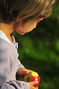 PETITE FILLE MANGEANT UNE POMME DANS SON JARDIN 