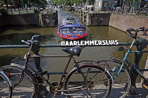 VELOS HOLLANDAIS ACCROCHE A LA BALUSTRADE DU PONT HAARLEMMERSLUIS SUR CANAL SINGEL ET BATEAU MOUCHE A LA SORTIE D'UNE ECLUSE SUR UN CANAL 