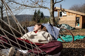 LORELEI FAIT LA SIESTE DANS SON HAMAC, ELLE A TOUT QUITTE POUR CONSTRUIRE ET HABITER SA CABANE EN BOIS AU MILIEU DE LA CREUSE, FRANCE 