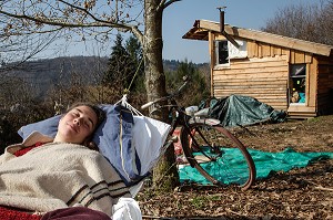 LORELEI FAIT LA SIESTE DANS SON HAMAC, ELLE A TOUT QUITTE POUR CONSTRUIRE ET HABITER SA CABANE EN BOIS AU MILIEU DE LA CREUSE, FRANCE 