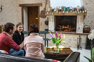 GROUPE D'AMIS PRENANT UN VERRE DANS UN CANAPE DEVANT UN FEU DE CHEMINEE, EURE-ET-LOIR, FRANCE 
