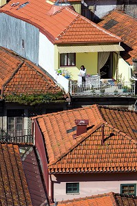 FEMME EN TRAIN D'ETENDRE SON LINGE SUR SON BALCON AU MILIEU DES TOITS DE TUILES ROUGES, VILA NOVA DE GAIA, PORTO, PORTUGAL 