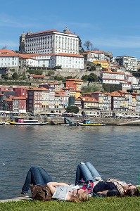 TOURISTES ALLONGES SUR LES BERGES DU DOURO FACE A LA VILLE DE PORTO, VILA NOVA DE GAIA, PORTUGAL 