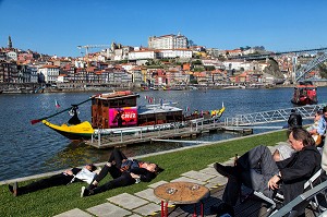 PETITE SIESTE APRES LA DEGUSTATION, PROMENEURS AU BORD DU DOURO DEVANT LES BATEAUX A FOND PLAT POUR LE TRANSPORT DU VIN (BARCOS RABELOS) AVEC LA VILLE ET LE PALAIS EPISCOPAL VILA NOVA DE GAIA, PORTO, PORTUGAL 