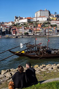 PROMENEURS AU BORD DU DOURO DEVANT LES BATEAUX A FOND PLAT POUR LE TRANSPORT DU VIN (BARCOS RABELOS) AVEC LA VILLE ET LE PALAIS EPISCOPAL VILA NOVA DE GAIA, PORTO, PORTUGAL 