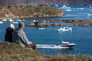 COUPLE ASSIS DEVANT LE SPECTACLE OFFERT PAR LES ICEBERGS FLOTTANT DANS LE FJORD DE LA BAIE DE NARSAQ, GROENLAND 