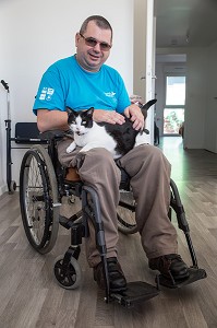 HOMME HANDICAPE PHYSIQUE DANS SON FAUTEUIL ROULANT CHEZ LUI AVEC SON CHAT, CHARTRES (28), FRANCE 