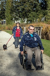 HOMME HANDICAPE PHYSIQUE DANS SON FAUTEUIL ROULANT AVEC SA FEMME ET SON CHIEN DANS LE PARC, CHARTRES (28), FRANCE 