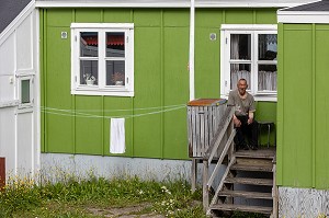 HABITANT FUMANT UNE CIGARETTE DEVANT SA MAISON TRADITIONNELLE EN BOIS DE COULEUR VERTE, VILLE DE QAQORTOQ, GROENLAND, DANEMARK 
