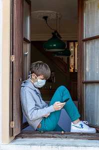 ADOLESCENT AVEC SON MASQUE DE PROTECTION SUR LA FENETRE DE SA MAISON, MESURES SANITAIRES DE PREVENTION, CONFINEMENT SUITE A L'EPIDEMIE DE CORONAVIRUS, RUGLES, NORMANDIE, FRANCE 