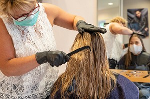 COIFFEUSE AVEC SON MASQUE DE PROTECTION ET SES GANTS EN TRAIN DE COIFFER UNE CLIENTE DANS UN SALON DE COIFFURE VIDE, RUGLES, NORMANDIE, FRANCE 