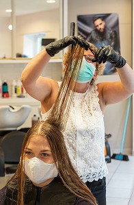 COUPE DES CHEVEUX AUX CISEAUX, COIFFEUSE AVEC SON MASQUE DE PROTECTION ET SES GANTS EN TRAIN DE COIFFER UNE CLIENTE DANS UN SALON DE COIFFURE VIDE, RUGLES, NORMANDIE, FRANCE 