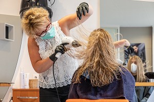 SECHAGE DES CHEVEUX, COIFFEUSE AVEC SON MASQUE DE PROTECTION ET SES GANTS EN TRAIN DE COIFFER UNE CLIENTE DANS LE SALON DE COIFFURE VIDE, RUGLES, NORMANDIE, FRANCE 