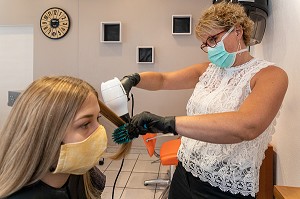 SECHAGE DES CHEVEUX, COIFFEUSE AVEC SON MASQUE DE PROTECTION ET SES GANTS EN TRAIN DE COIFFER UNE CLIENTE DANS LE SALON DE COIFFURE VIDE, RUGLES, NORMANDIE, FRANCE 