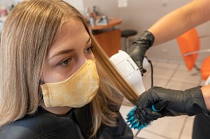 SECHAGE DES CHEVEUX, COIFFEUSE AVEC SON MASQUE DE PROTECTION ET SES GANTS EN TRAIN DE COIFFER UNE CLIENTE DANS LE SALON DE COIFFURE VIDE, RUGLES, NORMANDIE, FRANCE 