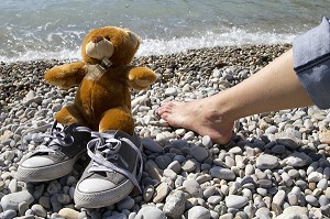 TEDDY L'OURS EN PELUCHE S'AMUSANT SUR UNE PLAGE DE GALETS 