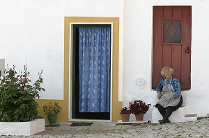 PORTUGAISE AU PIED DE SA PORTE DE MAISON SUR LES MARCHES DE L'ENTREE, VILLAGE DE TERENA, ALENTEJO, PORTUGAL 