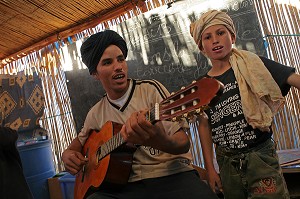 INSTITUTEUR BERBERE JOUANT DE LA GUITARE A SES ELEVES, CLASSE D'ENFANTS NOMADES, ASSOCIATION POUR LE DEVELOPPEMENT DE LA VIE NOMADE DANS LA REGION DE ZAGORA, PEUPLE BERBERE, MAROC, MAGHREB, AFRIQUE 