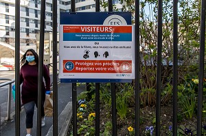 AFFICHAGE SYMPTOMES DU COVID 19 ET PATIENTE AVEC UN MASQUE ET DES GANTS SORTANT DE L'HOPITAL SAINT ANTOINE, PARIS, ILE-DE-FRANCE 