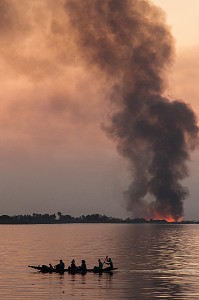 TRAVERSEE DE PIROGUES DEPUIS LA MAURITANIE SUR LE FLEUVE AVEC LES FEUX DE CANNE A SUCRE SUR FOND DE COUCHER DE SOLEIL, DAGANA, SENEGAL, AFRIQUE DE L'OUEST 