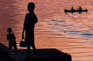 JEU D'ENFANTS DEVANT LE FLEUVE AVEC LES FEU DE CANNE A SUCRE SUR FOND DE COUCHER DE SOLEIL, DAGANA, SENEGAL, AFRIQUE DE L'OUEST 