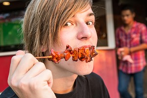 JEUNE EUROPEEN DECOUVRANT LES SAVEURS EPICEES D'UNE BROCHETTE DE PORC, BANG SAPHAN, THAILANDE, ASIE 
