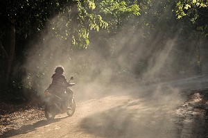 JEUNE FEMME TRAVERSANT LA JUNGLE A SCOOTER, DANS LA POUSSIERE, REGION DE BANG SAPHAN, THAILANDE, ASIE 