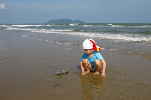ENFANT SUR LA PLAGE JOUANT AVEC UNE BOUTEILLE EN PLASTIQUE REJETE PAR LA MER 