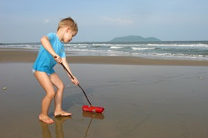ENFANT SUR LA PLAGE JOUANT AVEC UNE BOUTEILLE EN PLASTIQUE REJETE PAR LA MER 