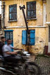 SCENE DE RUE AVEC MOTO DEVANT UNE MAISON JAUNE AVEC UNE CHEMINEE QUI SORT PAR LA FENETRE, RUE MERKEZ HASTANE, VILLE D'AYVALIK SUR LES BORDS DE LA MER EGEE, RIVIERA DES OLIVIERS, NORD D’IZMIR, TURQUIE 