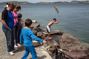 RETOUR DE LA PECHE, TOURISTES DEVANT LE PECHEUR EN TRAIN DE BATTRE DES POULPES, SORTE DE PIEUVRE, PORT DE FOCA SUR LA MER EGEE,  RIVIERA DES OLIVIERS, NORD D’IZMIR, TURQUIE 