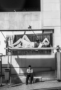 FEMME ASSISE DANS UN ABRIS BUS AVEC LA PHOTO D'UNE PUBLICITE DE MANNEQUIN ALLONGEE AU DESSUS D'ELLE, FUNCHAL, MADERE, PORTUGAL 